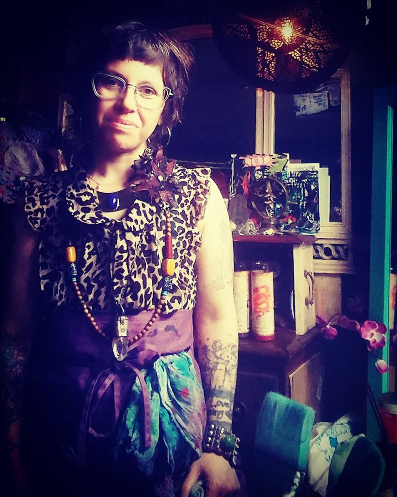 a portrait of Alanna Kibbe in her Studio. she wears a tanktop with animal prints and a light blue bottom, and a pair of glasses with transparent rims
